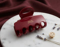 A glossy deep red hair claw clip with gold lettering reading 'Barette La France', displayed on a white marble tray with lavender sprigs and a gold hair pin against a draped burgundy fabric background.